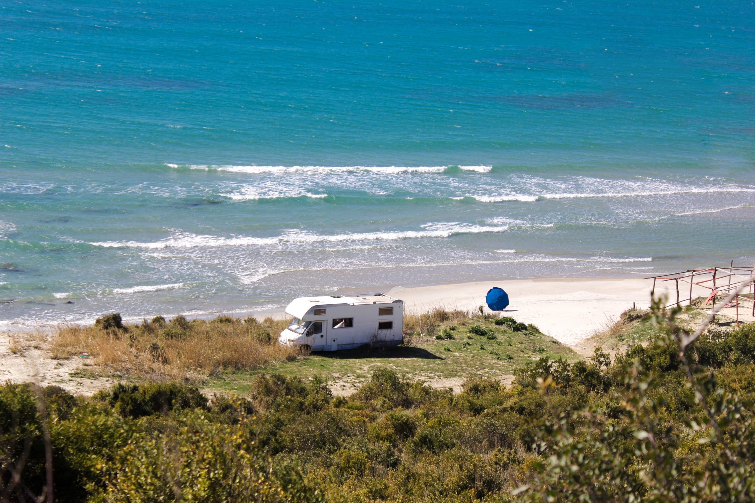 Camper set near a sandy beach with sun shelter and towels